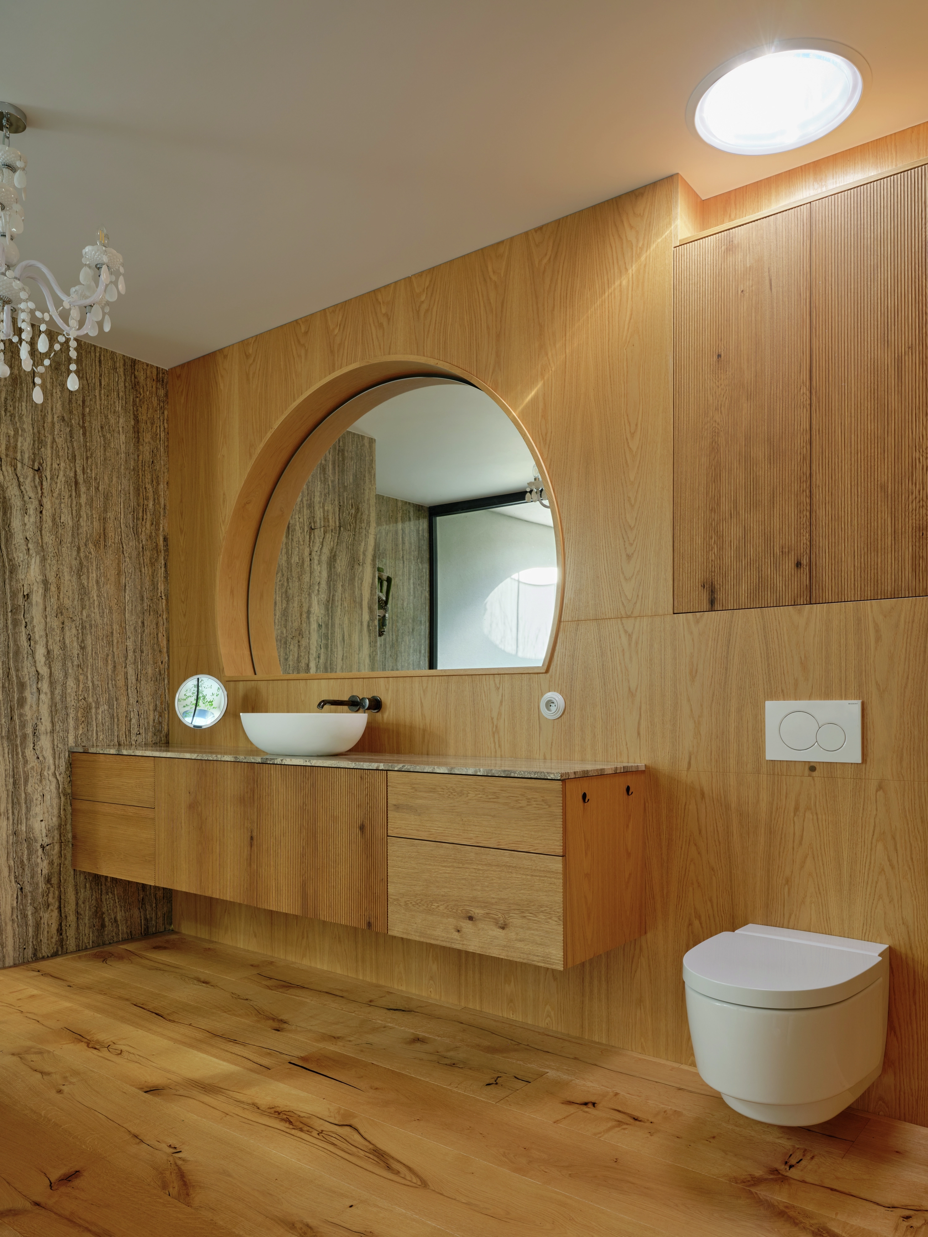 Modern wooden bathroom with floating vanity, round mirror and ceiling daylight shaft.