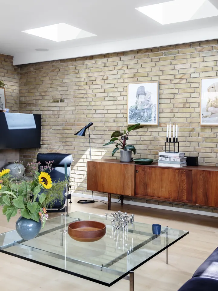 Tuğla duvarlar, ahşap büfe, cam sehpa ve çatı pencerelerinden gelen bol doğal ışık ile bezenmiş, Orta Çağ'dan modern bir oturma odası.