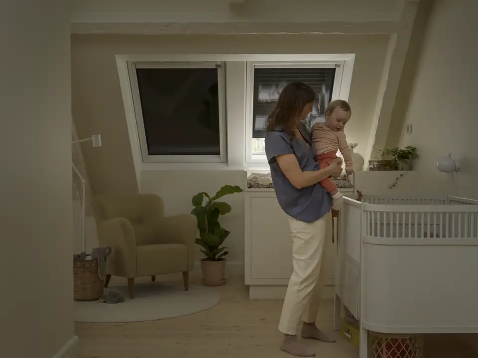 Una donna prepara il suo bambino per la nanna in cameretta con le tapparelle per finestre per tetti abbassate per oscurare.