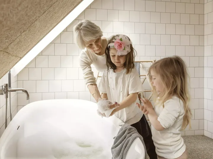 Kinder spielen mit Seifenblasen bei einer Badewanne unter einem VELUX Dachflächenfenster in einem gefliesten Badezimmer.