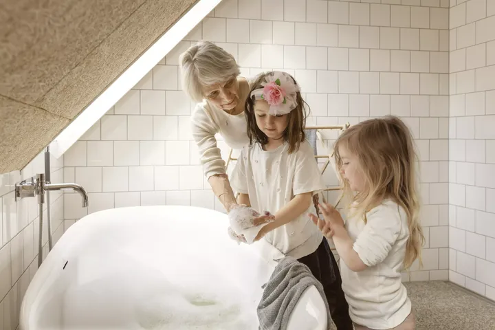 Oma steht mit ihren Enkelinnen vor einer Badewanne voller Schaum unter einer Dachschräge | VELUX Magazin