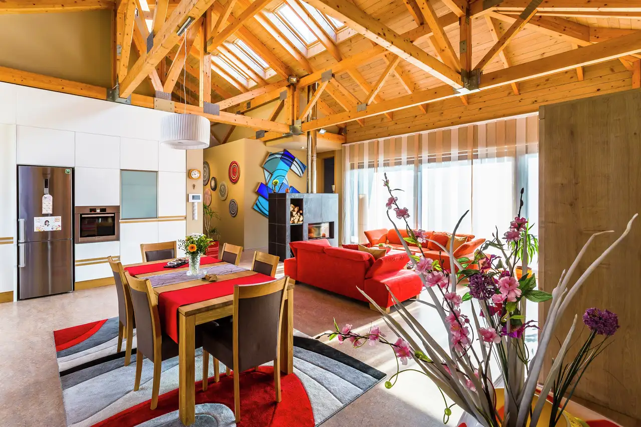 Séjour lumineux avec fenêtres de toit VELUX, poutres en bois et touches de rouge créant une ambiance chaleureuse et dynamique