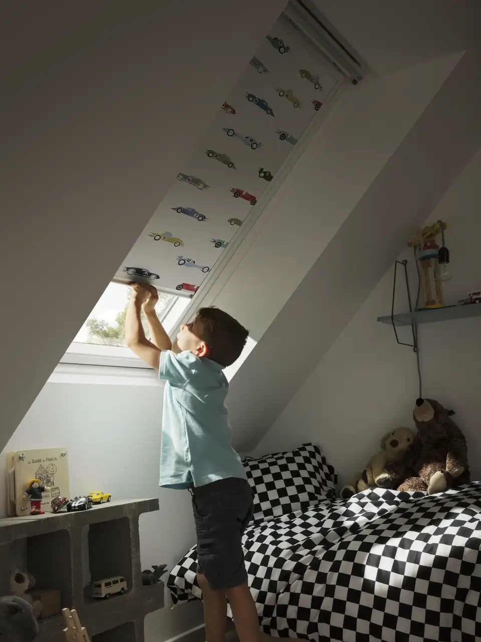 Chambre d’enfant avec fenêtre de toit et store occultant à enrouleur manipulé par un enfant.