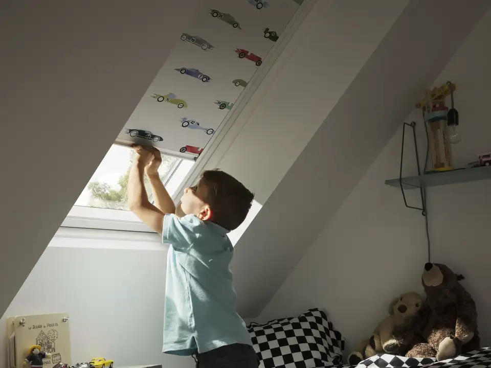 Child's room with sloped ceiling and VELUX roof window, boy reaching up.