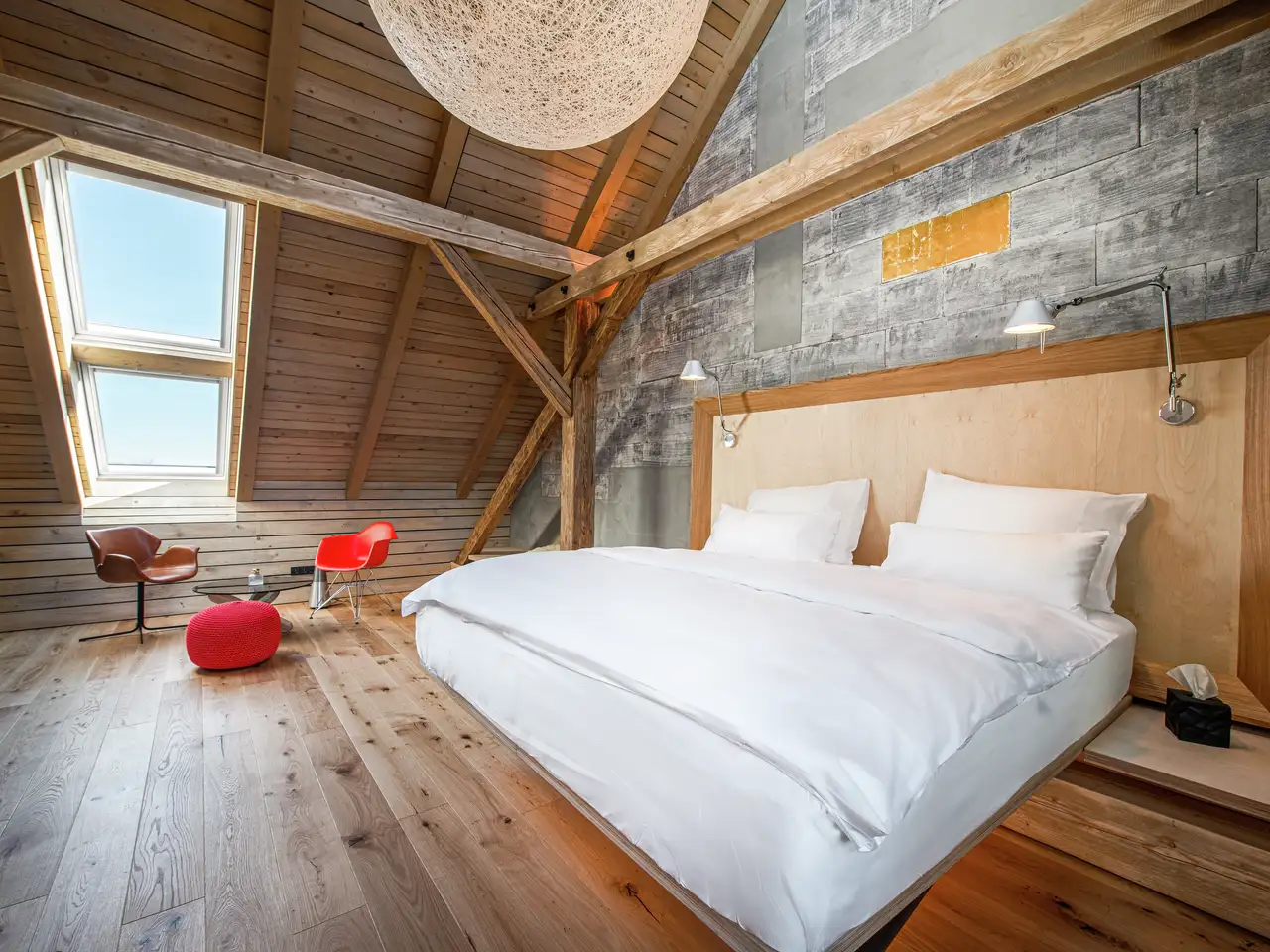 Camera da letto con soffitto spiovente, pavimento in parquet, parete in pietra, finestra per tetti VELUX e travi a vista.