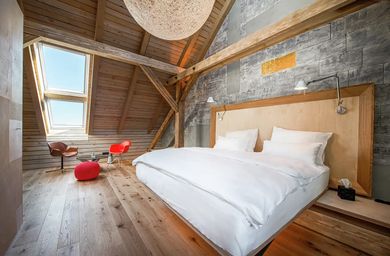 chambre à coucher avec plafond rampant, parquet, mur en pierre, fenêtre de toit VELUX et poutres apparentes