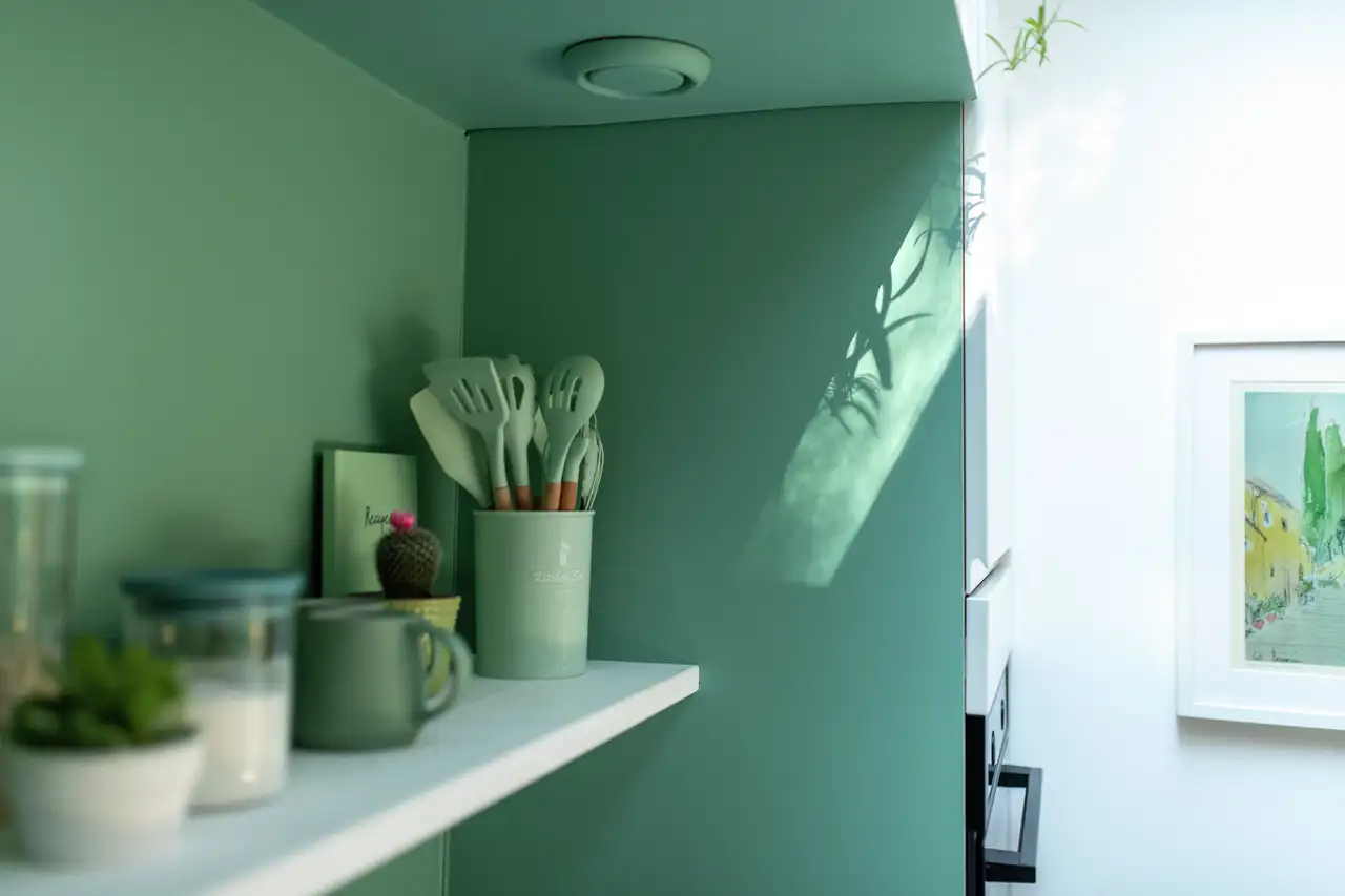 Detail einer pastellgrünen Küchenecke im Danish-Pastel-Stil mit Küchenutensilien, offenen Regalen und sanftem Tageslichtspiel an der Wand | VELUX Magazin