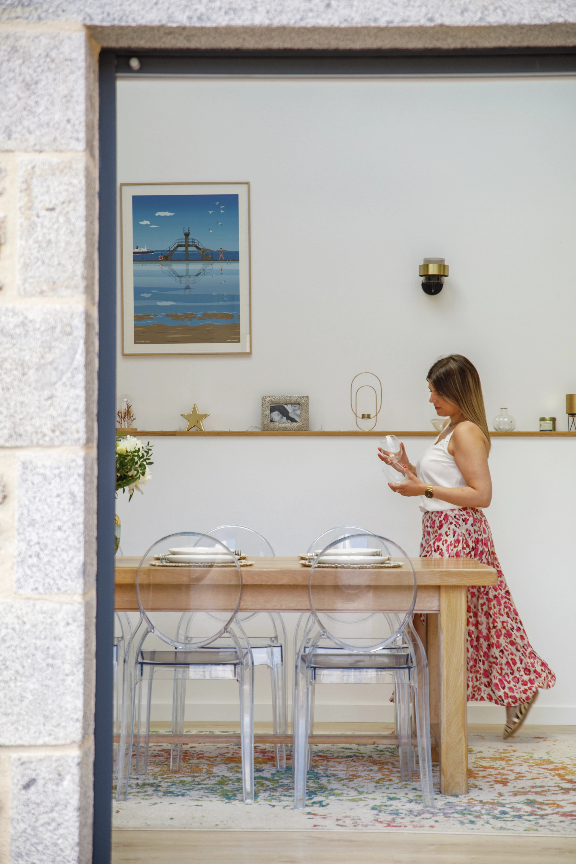 Salle à manger moderne avec table en bois, chaises transparentes et art mural nautique.