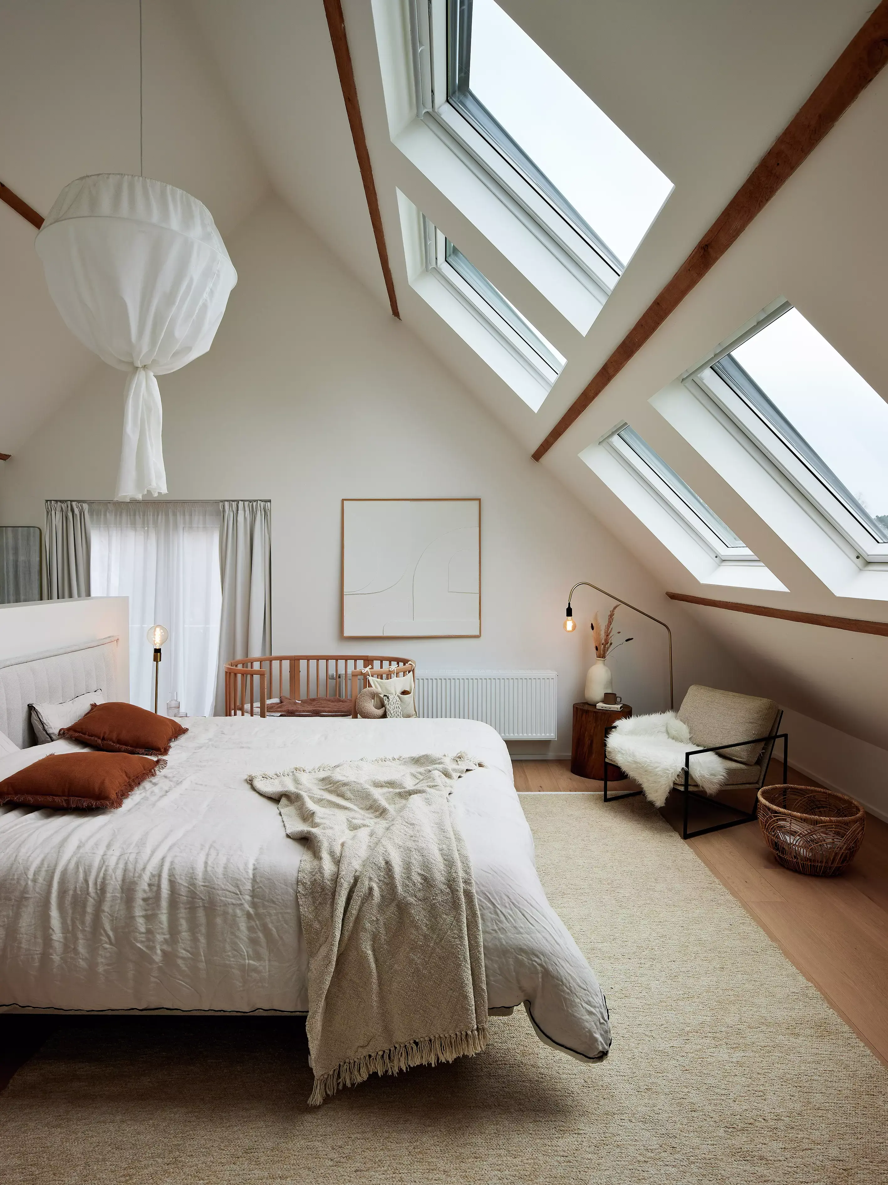 Ampia camera da letto mansarda con finestre per tetti VELUX, travi in legno e arredamento accogliente.