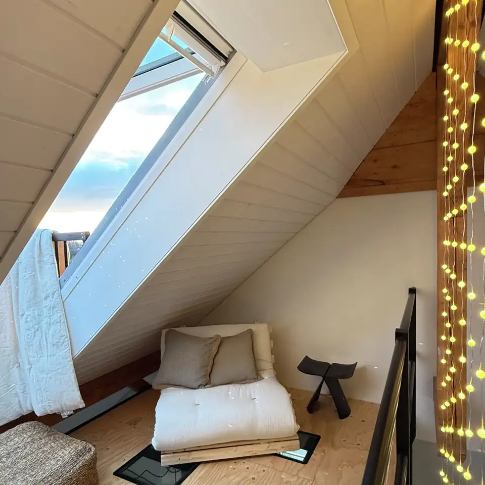 Dormitorio en el ático con un sillón y una ventana balcón VELUX abierta para ventilar 
