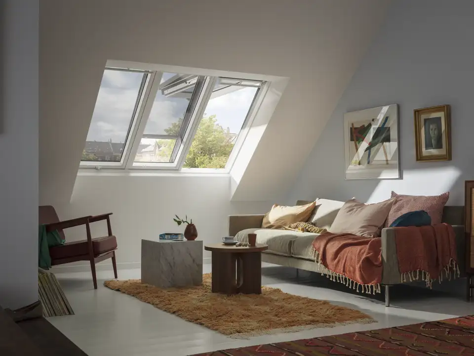 Dnevna soba na podstrešju s poševnim stropom in strešnim oknom VELUX, z zunanjimi mrežastimi senčili in domačo opremo.