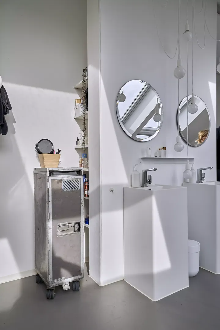 Minimalistisches Badezimmer mit weißen Wänden, runden Spiegeln und einem Metallrollwagen.
