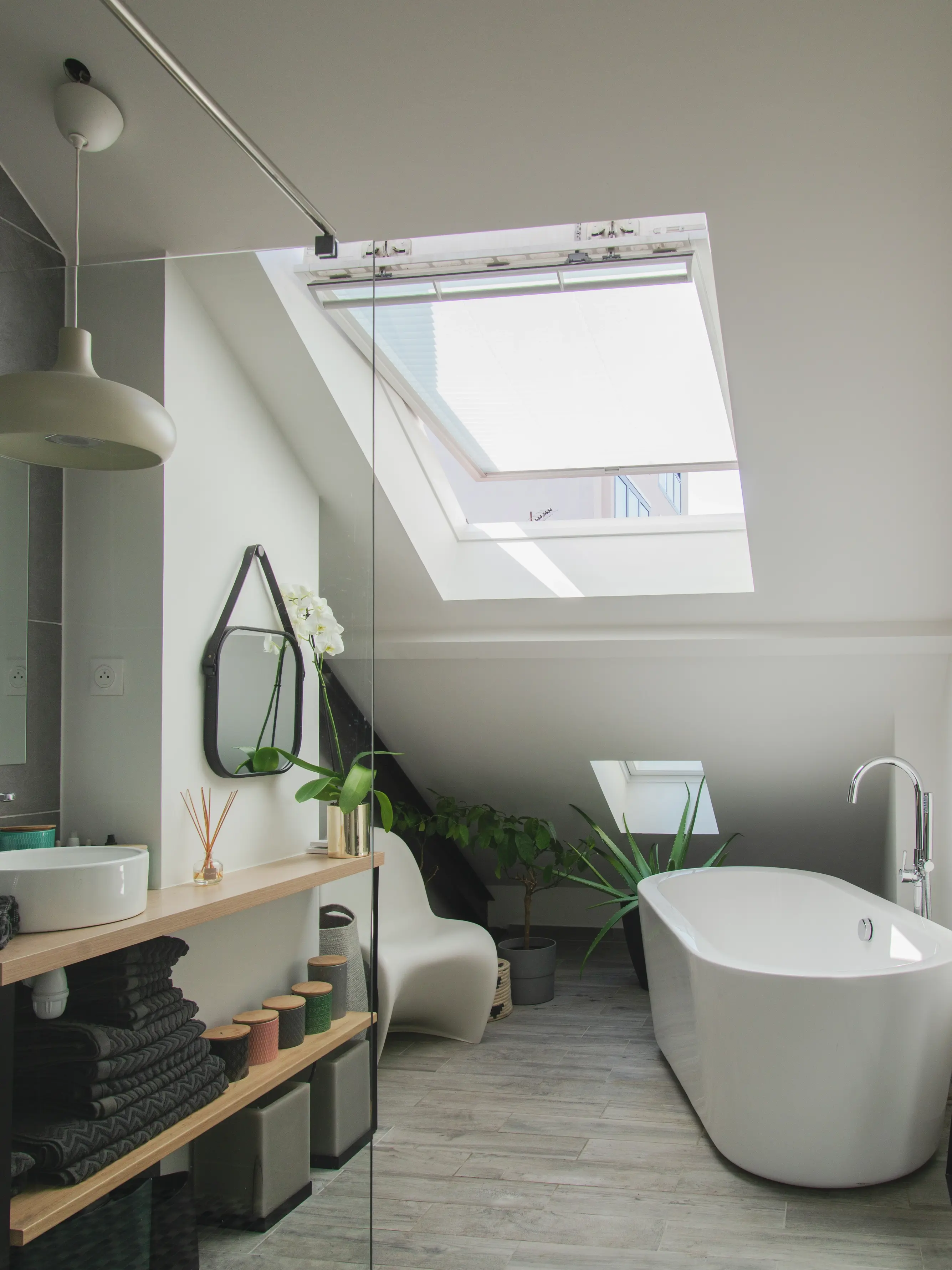 Salle de bain moderne avec fenêtre de toit VELUX, baignoire indépendante et plantes vertes.