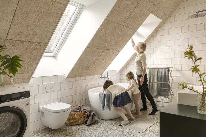 Frau mit Kindern in einem hellen Badezimmer mit VELUX Dachflächenfenster und freistehender Badewanne.