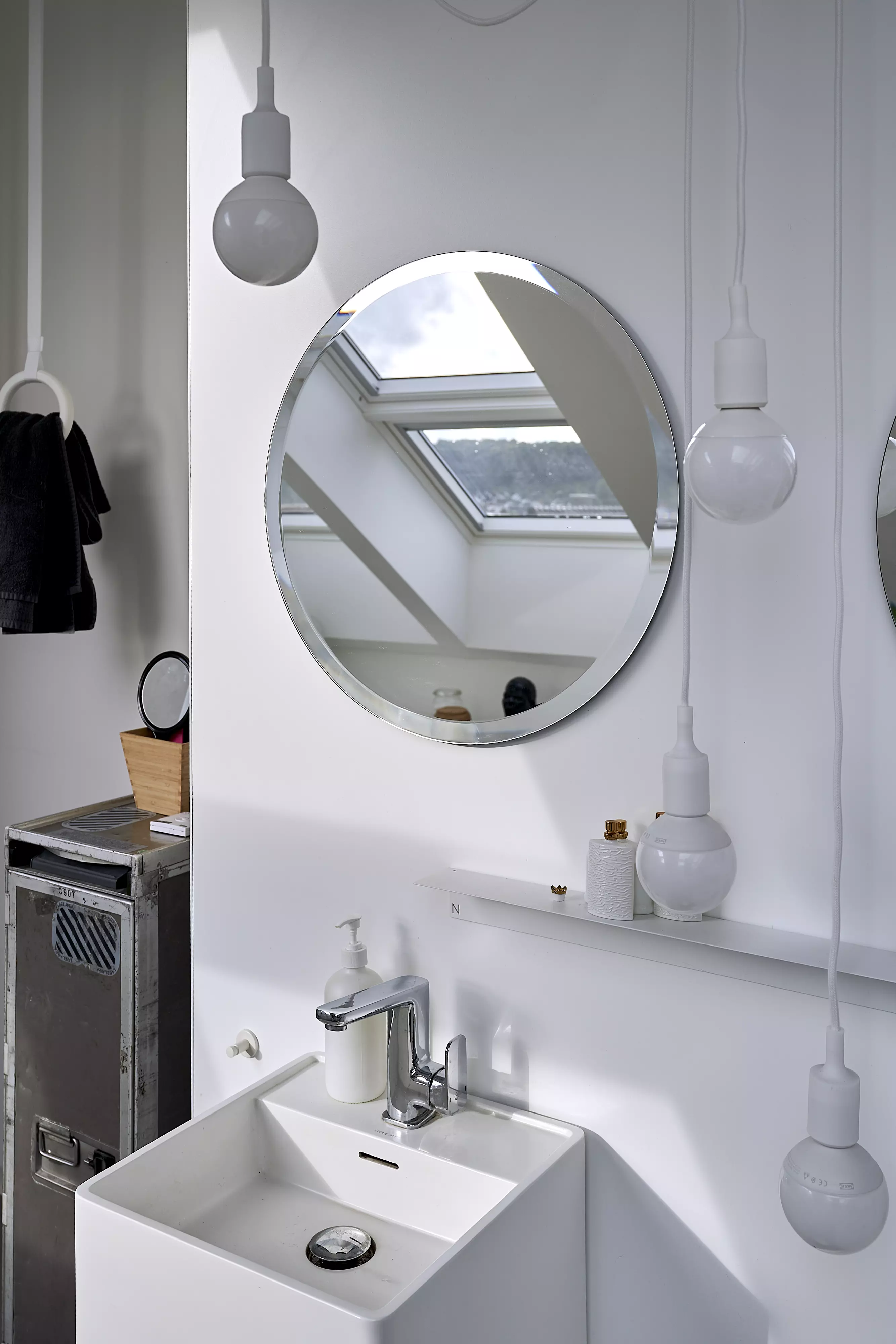 Modernes Badezimmer mit weißem Waschbecken, rundem Spiegel und VELUX Dachflächenfenster.