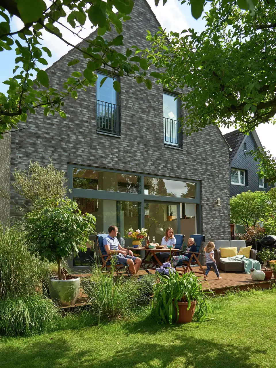 Une famille se détend sur une terrasse, devant une maison moderne avec de grandes fenêtres - VELUX