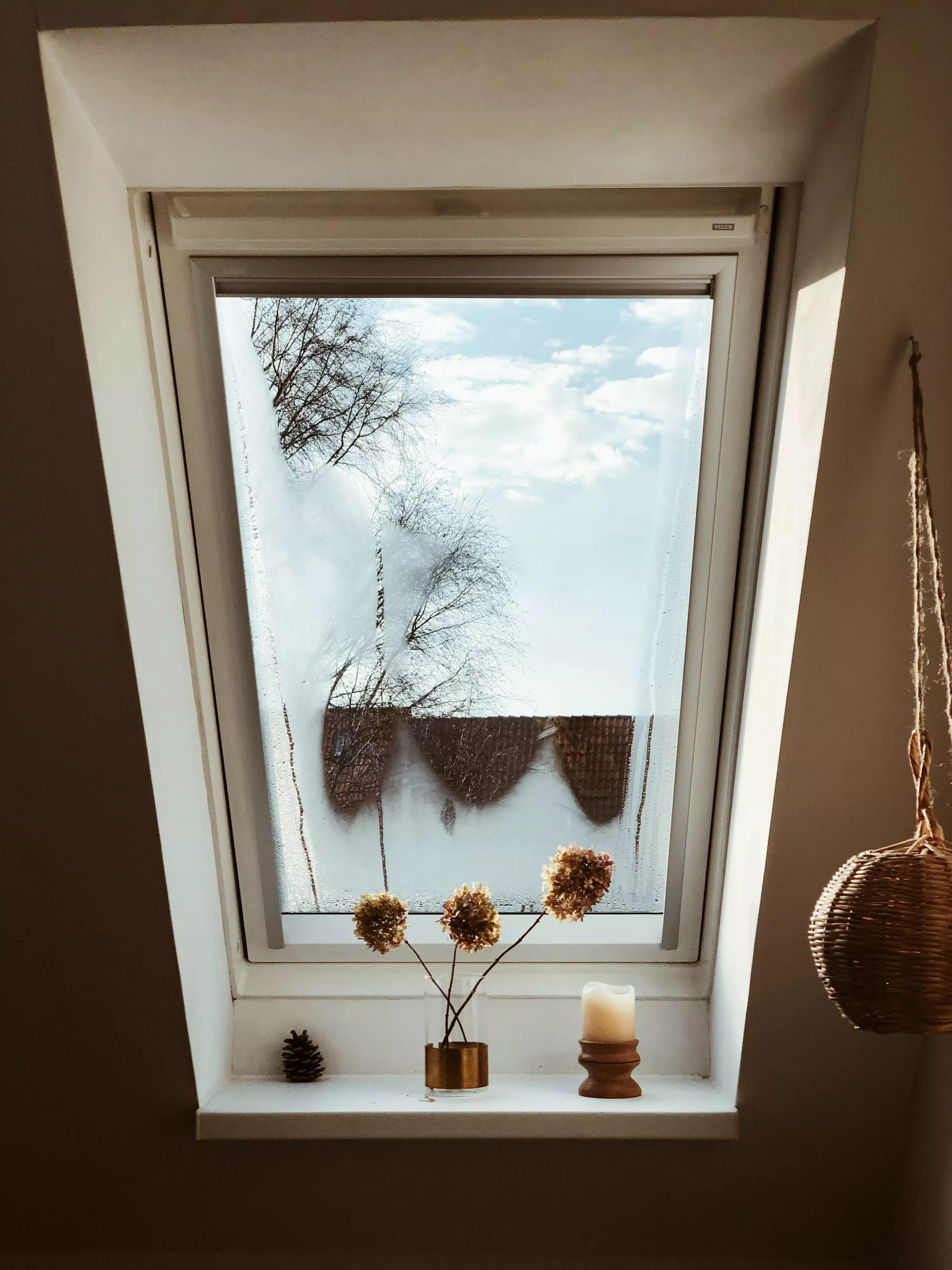 Fenêtre VELUX dans le comble avec des objets décoratifs sur le rebord, montrant le ciel et les arbres.