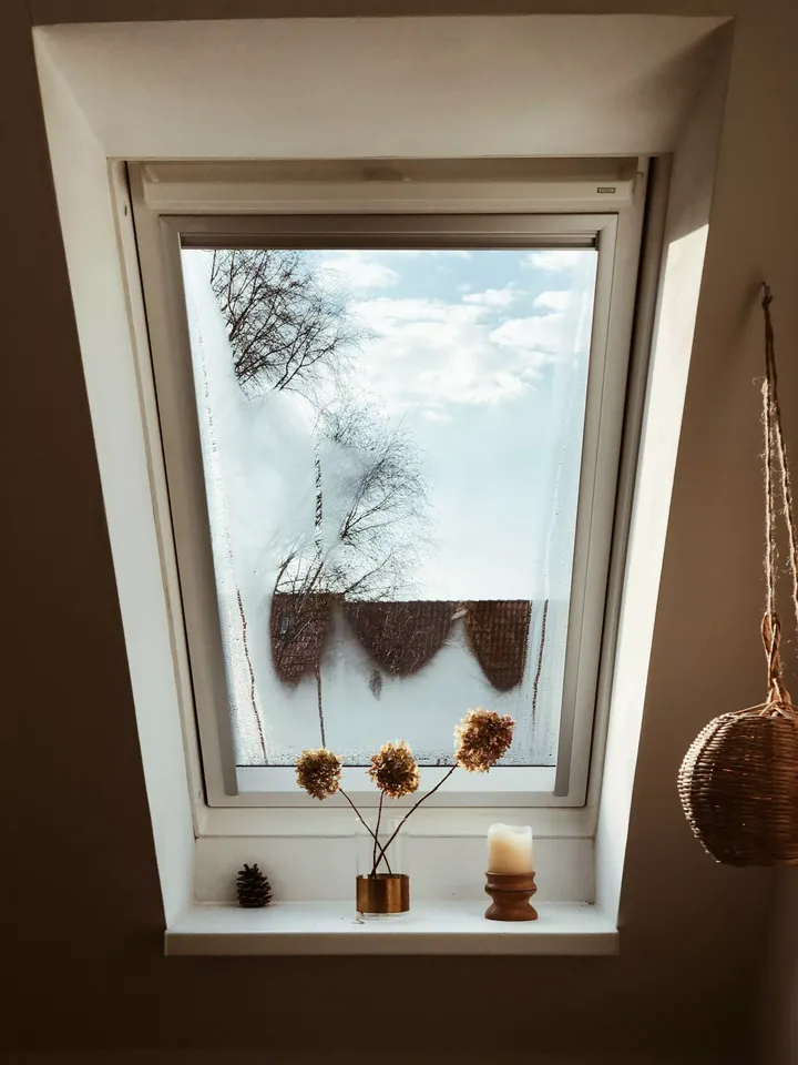VELUX-Fenster im Dachbodenraum mit dekorativer Vase, Kerze und Tannenzapfen auf der Fensterbank.
