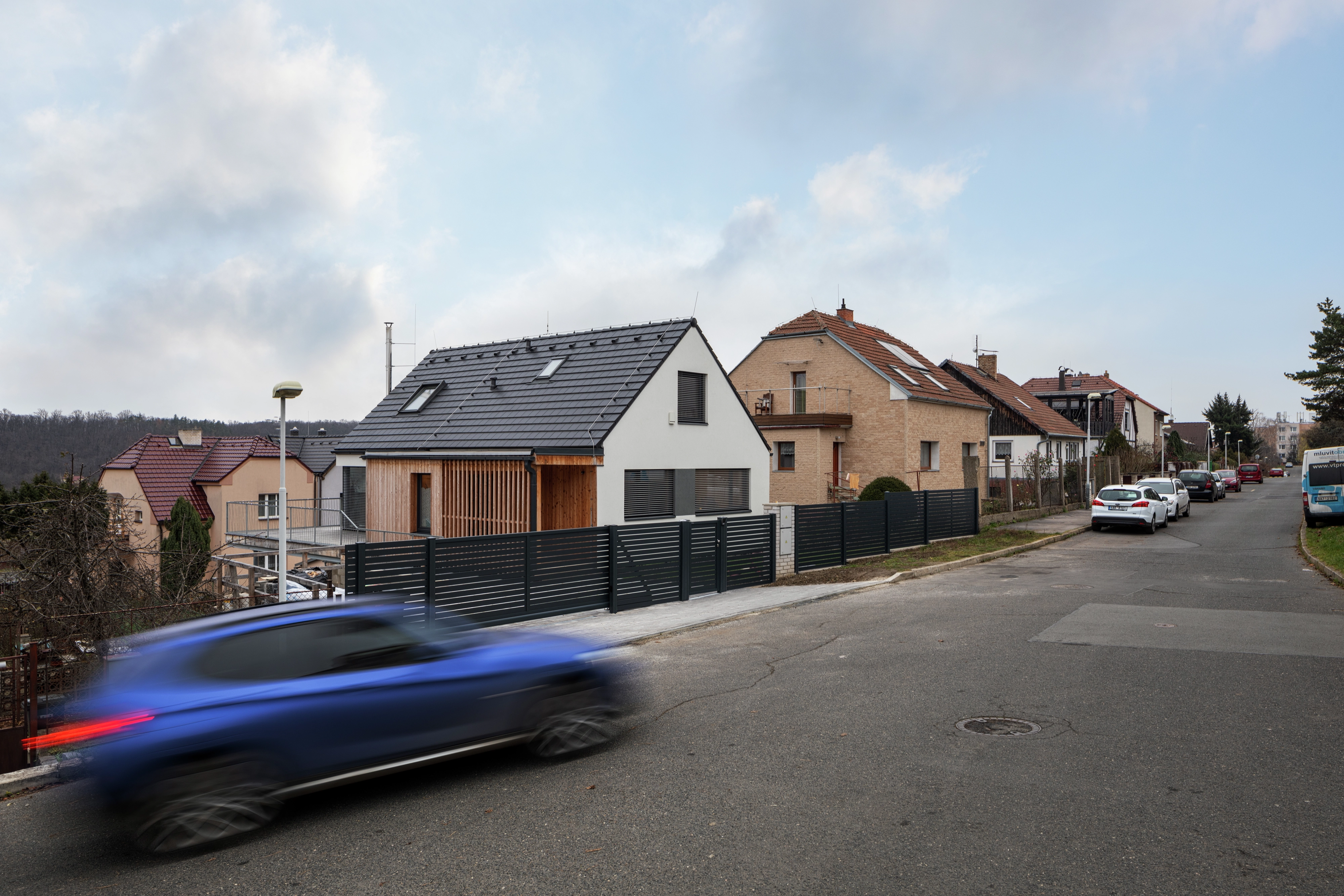 Modern residential street with houses, cars, and a moving blue car.