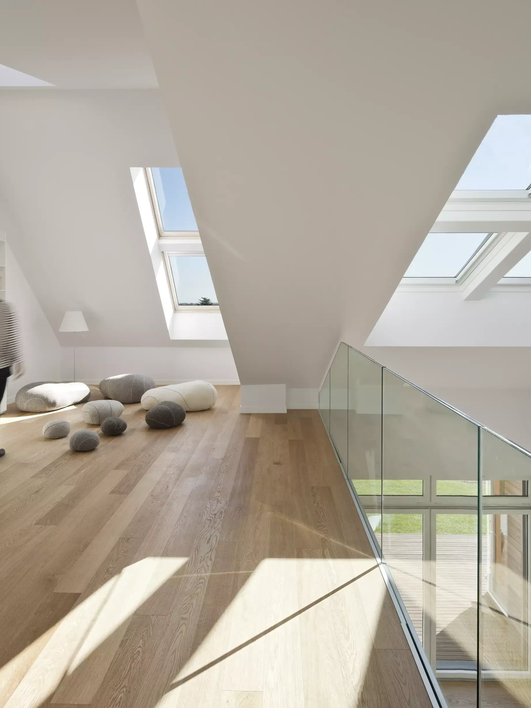 Mansarda moderna con finestra VELUX, pavimento in legno e balaustra in vetro.