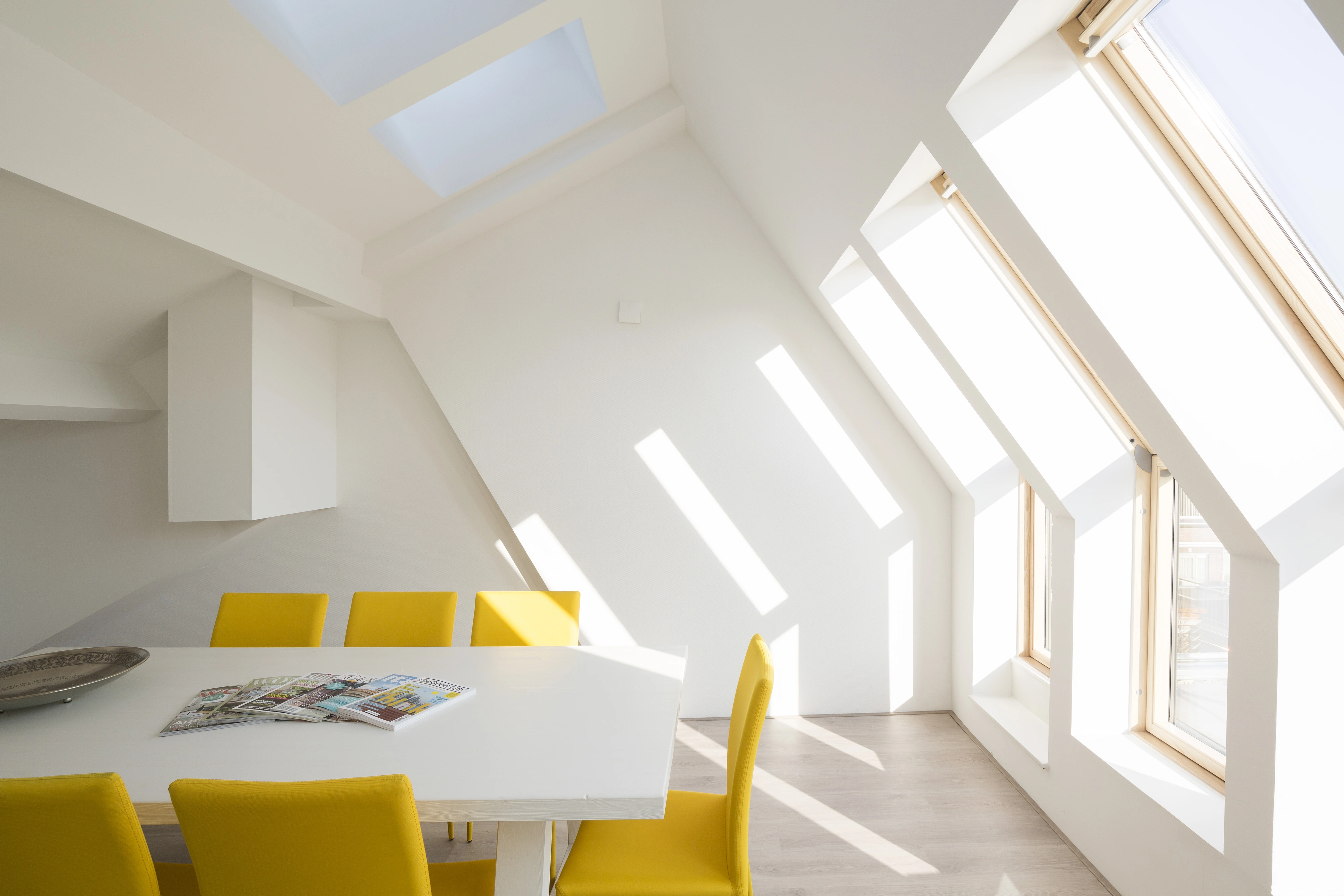 Attic dining room with sloped ceiling and large roof windows, bright and modern.