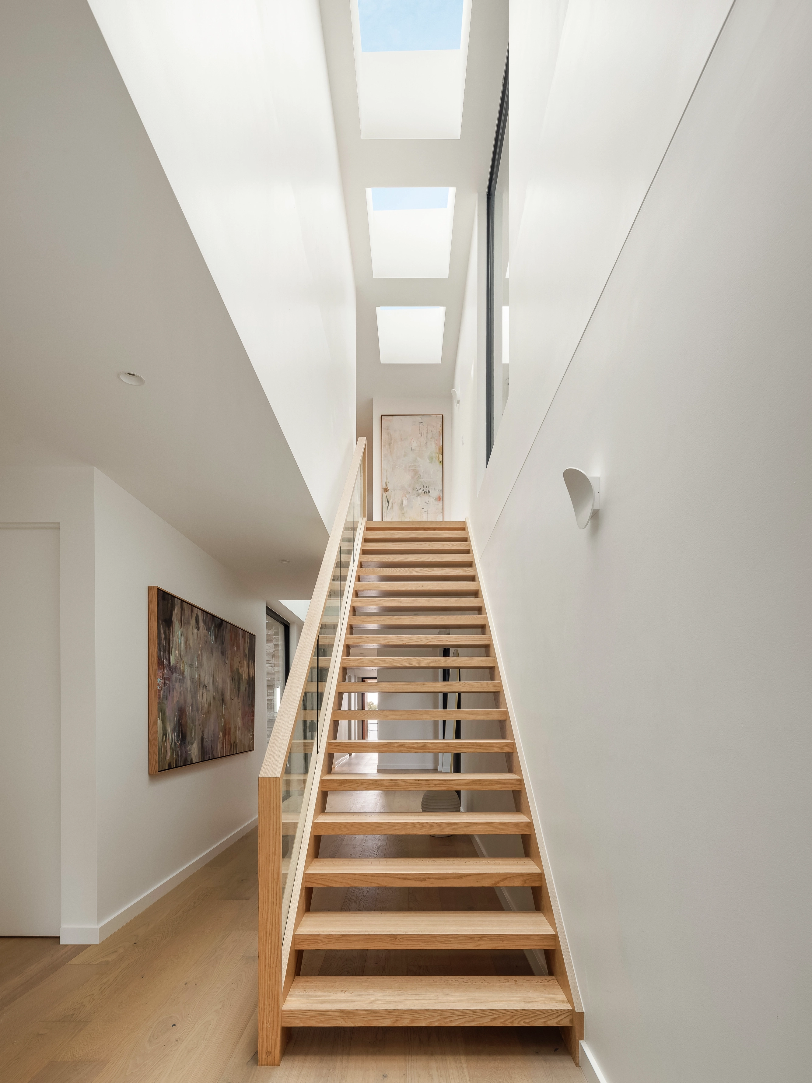 Modern stairwell lit by multiple VELUX flat roof windows above a light wooden staircase.