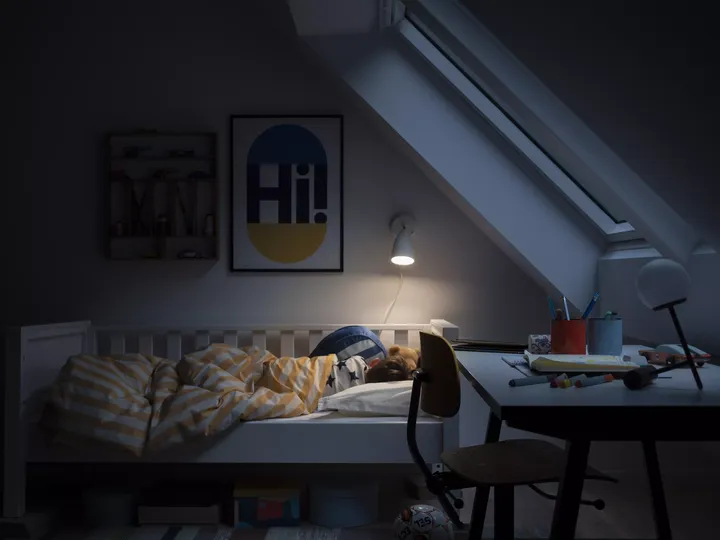 Kind schläft unter Verdunkelungsrollos mit kleiner Lampe am Bett zwecks Zeitumstellung | VELUX Magazin