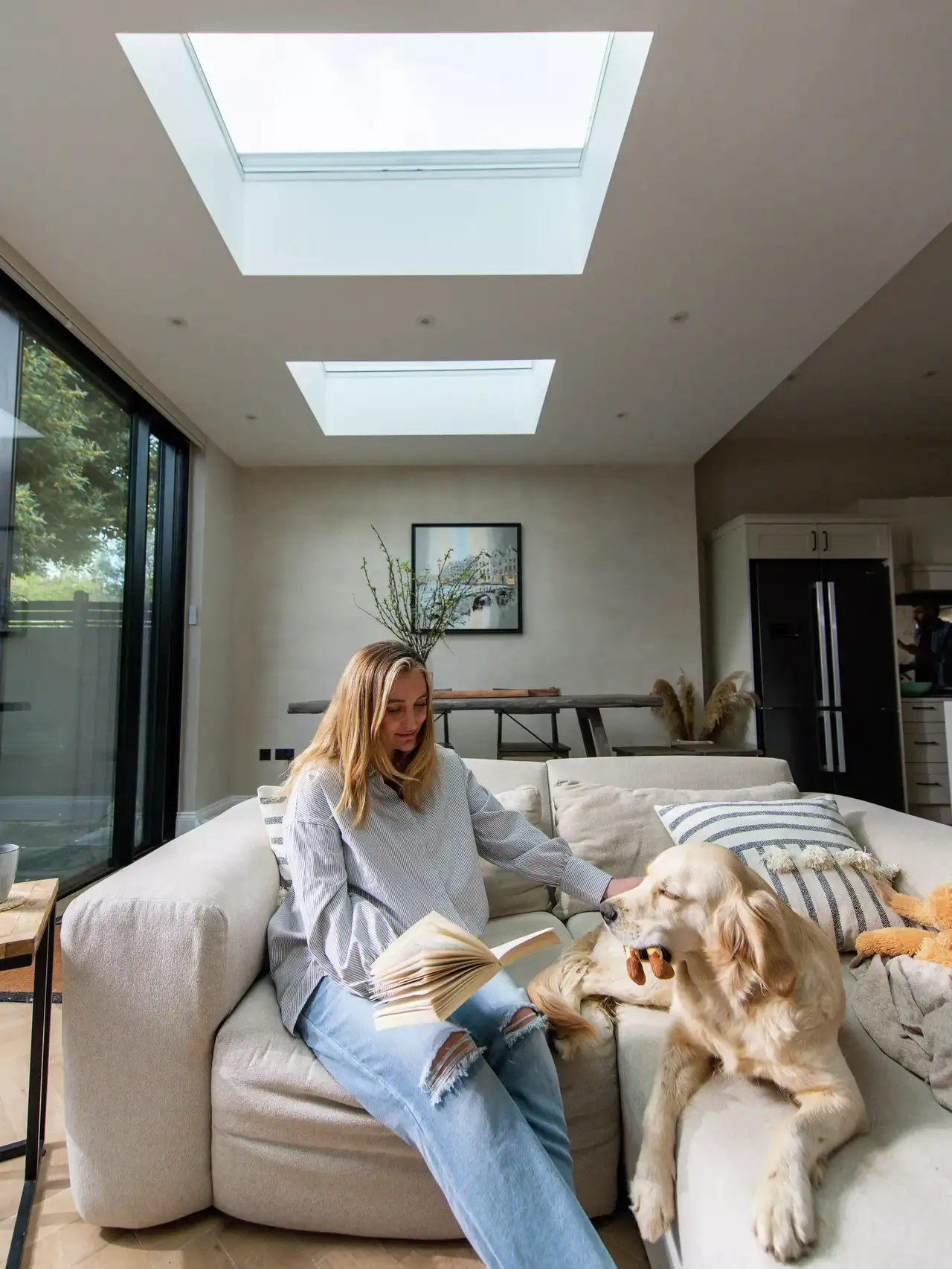 Gemütliches Wohnzimmer mit VELUX Dachflächenfenstern, Person beim Lesen und einem Hund auf dem Sofa.