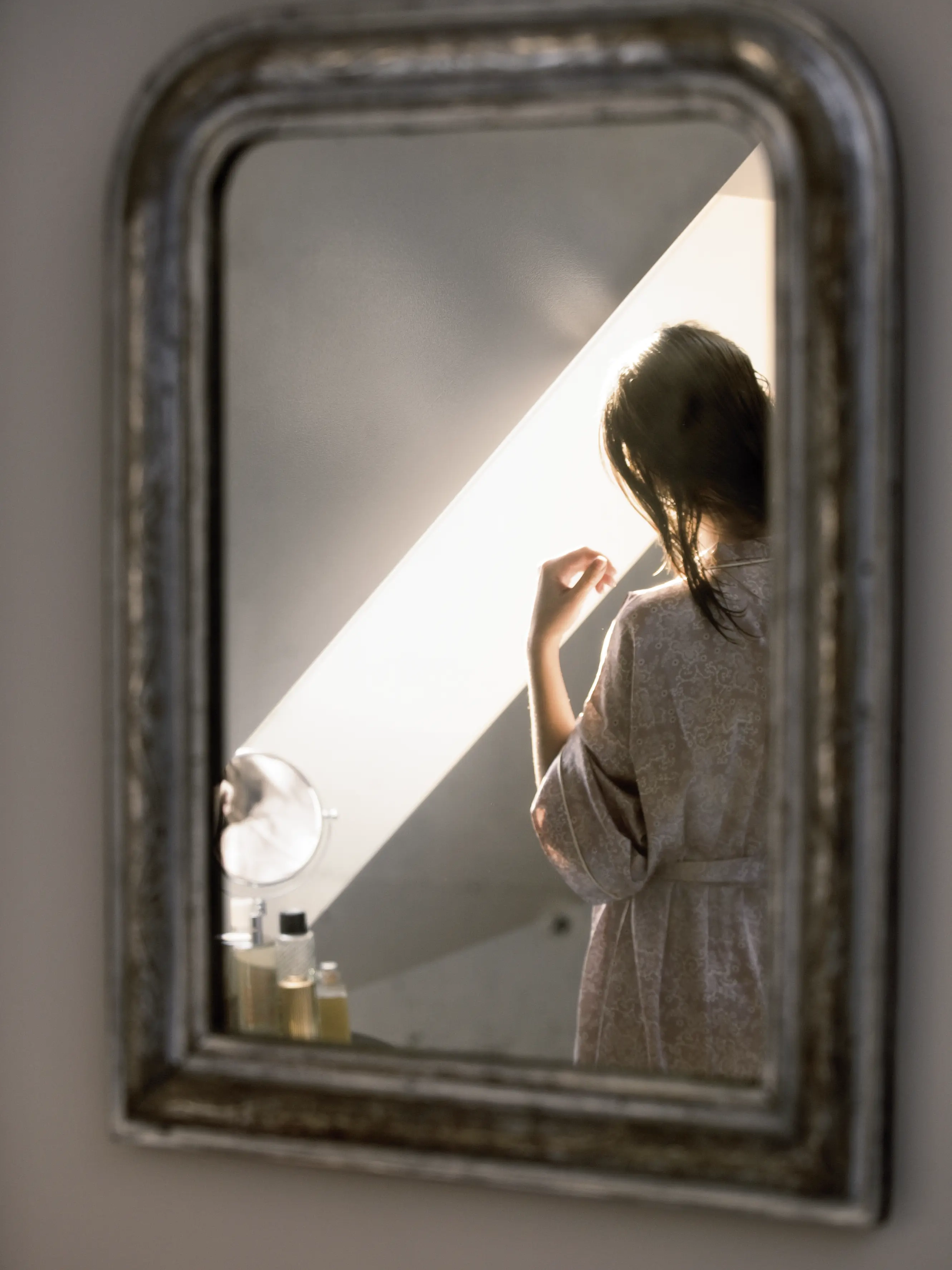 Femme reflétée dans un miroir dans une chambre mansardée avec un plafond incliné et une fenêtre de toit.