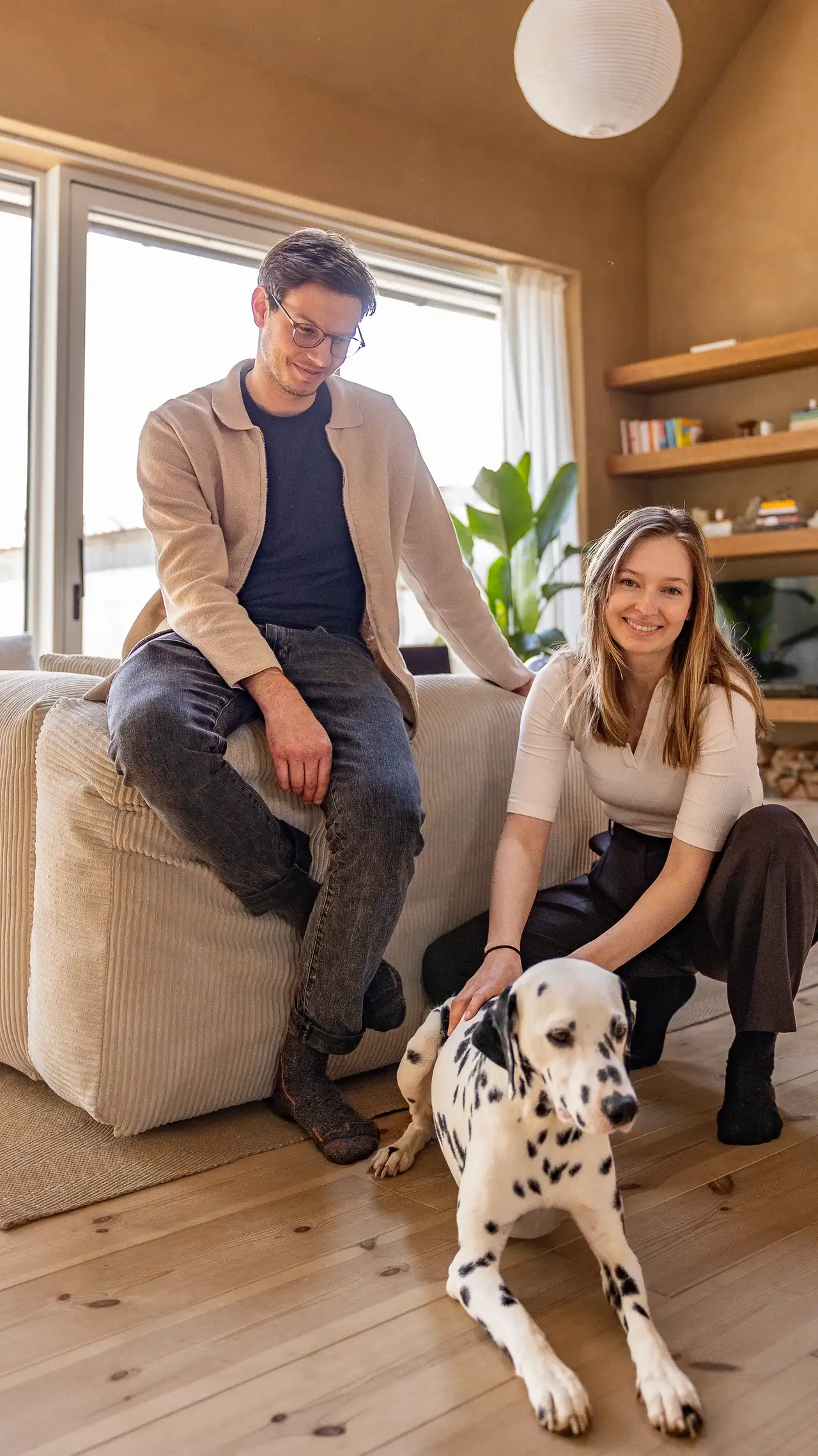 Ein Paar mit ihrem Dalmatiner in einem hellen Wohnzimmer, das von Tageslicht durch große Fenster erleuchtet wird. | VELUX Magazin