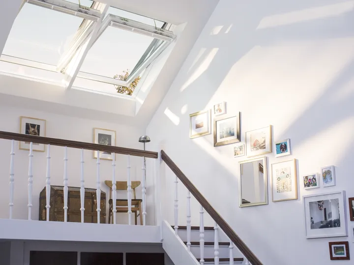 Von zwei großen Dachfenstern in Sonnenlicht getauchte Bilder an der Dachschräge entlang einer Treppe | VELUX Magazin