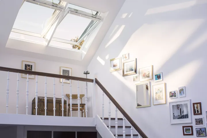 Von zwei großen Dachfenstern in Sonnenlicht getauchte Bilder an der Dachschräge entlang einer Treppe | VELUX Magazin