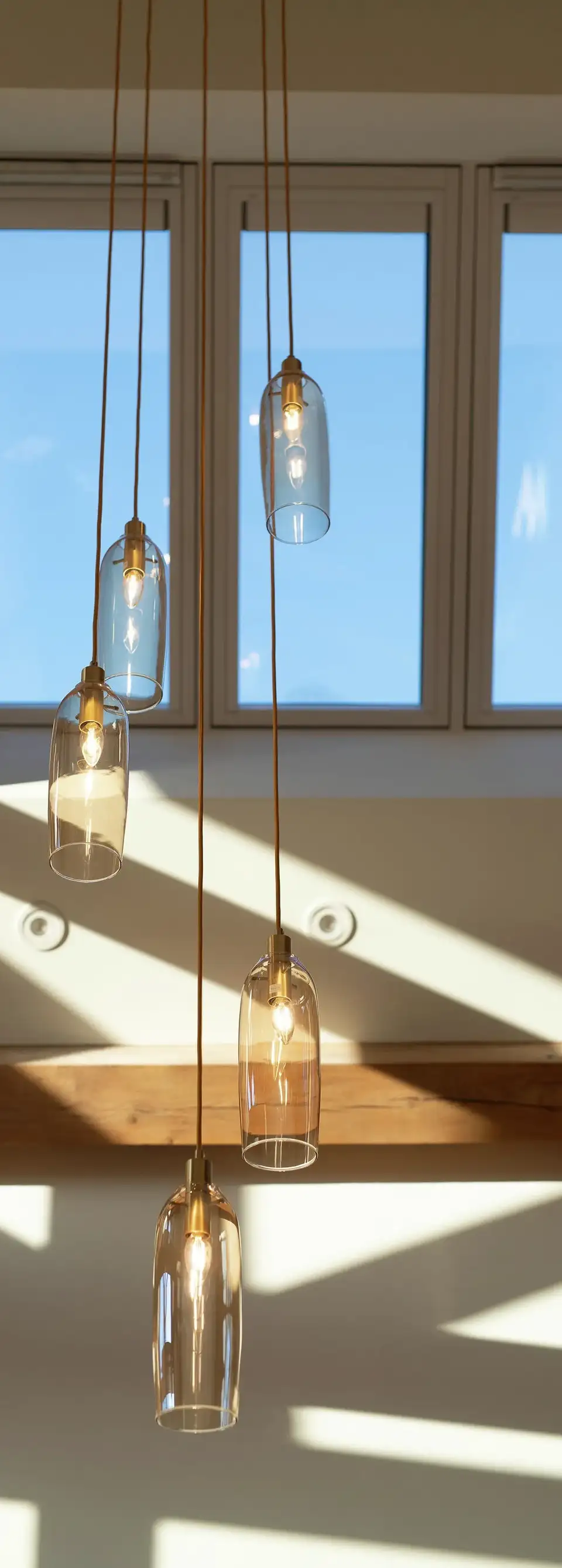 Suspensions en verre transparent à hauteurs variées sous un plafond incliné avec fenêtres de toit VELUX.