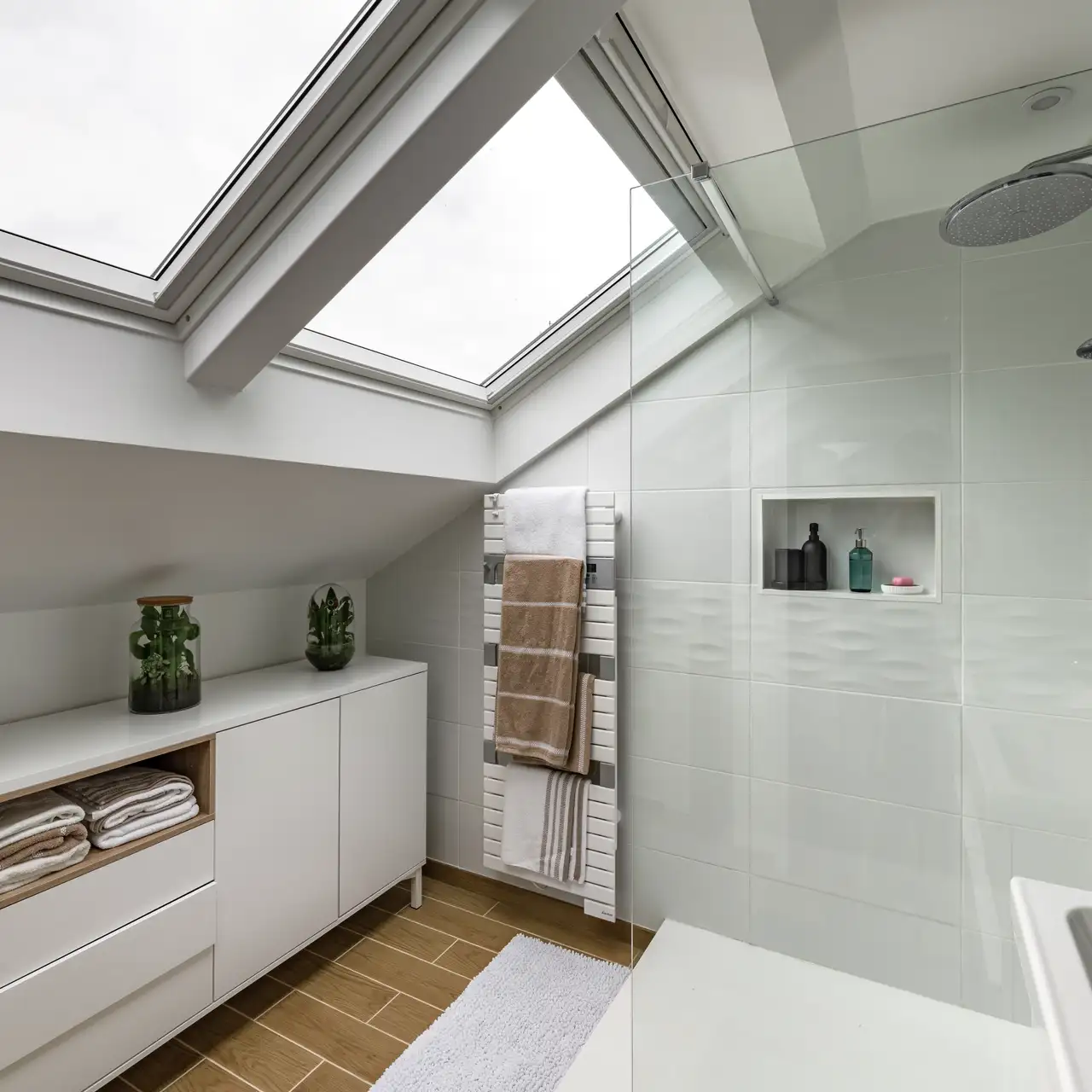 Salle de bain sous combles avec meuble bas placé contre un mur incliné, sous deux grandes fenêtres de toit