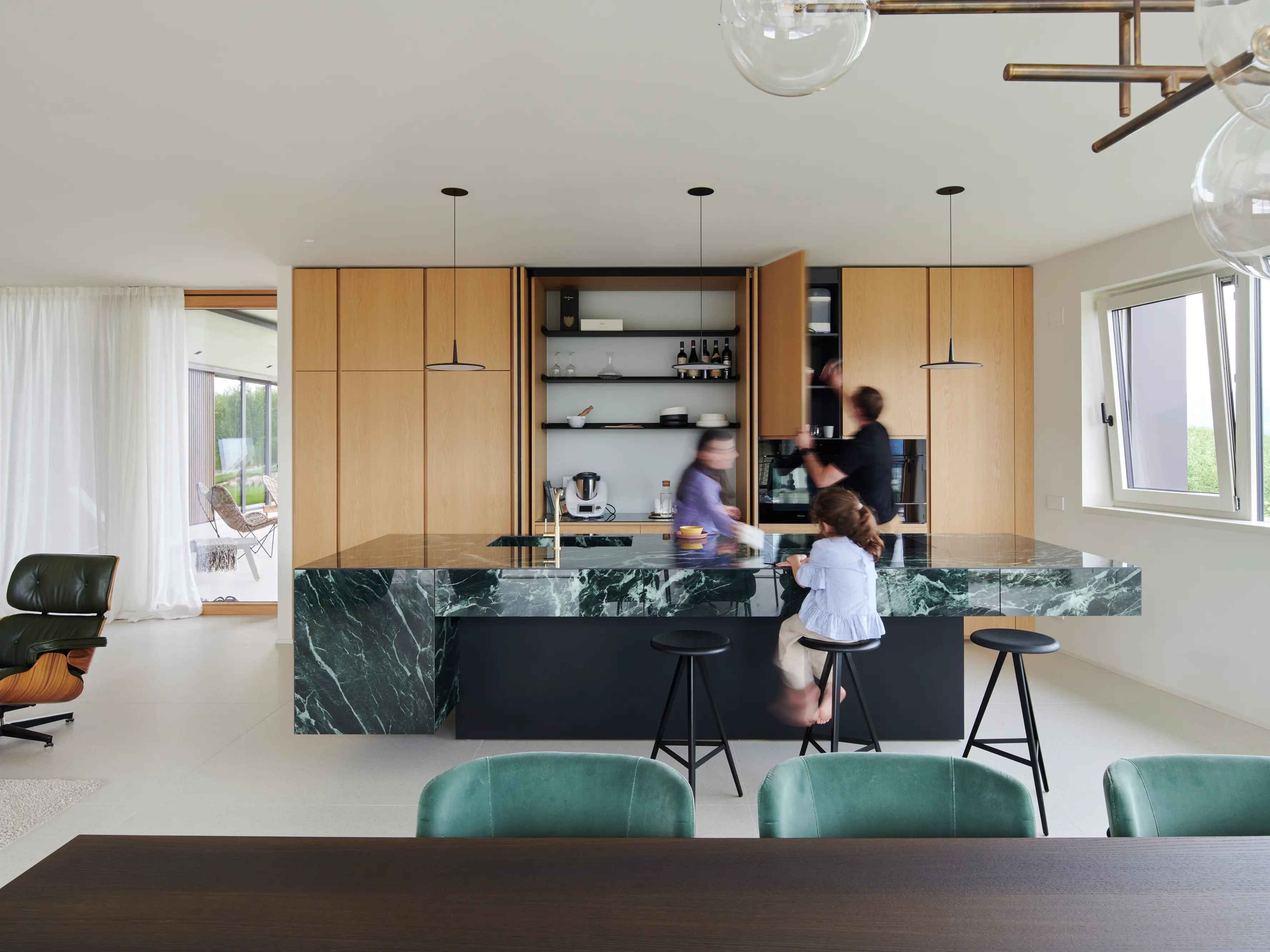 Cuisine moderne spacieuse avec des armoires en bois, un îlot en marbre vert et une famille qui interagit.