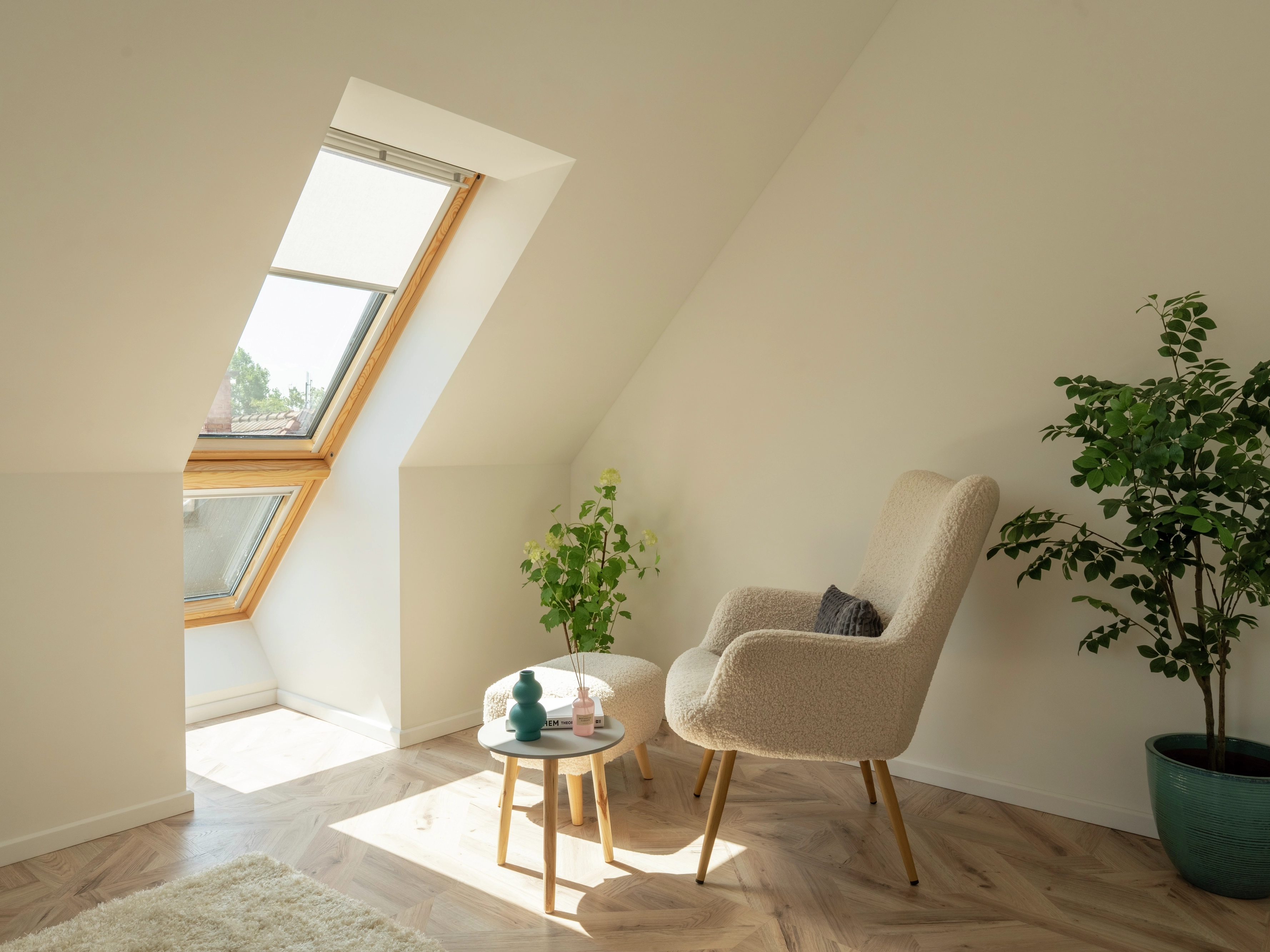 Attic room with sloped ceiling, VELUX roof window, armchair, and plants.