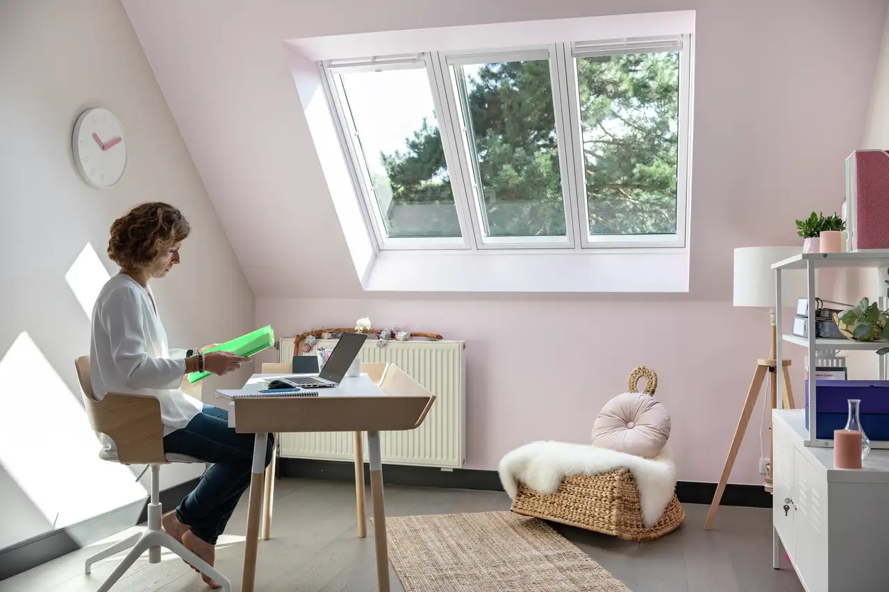 Donna alla scrivania nel suo home office in mansarda, con finestra per tetti 3in1 VELUX.