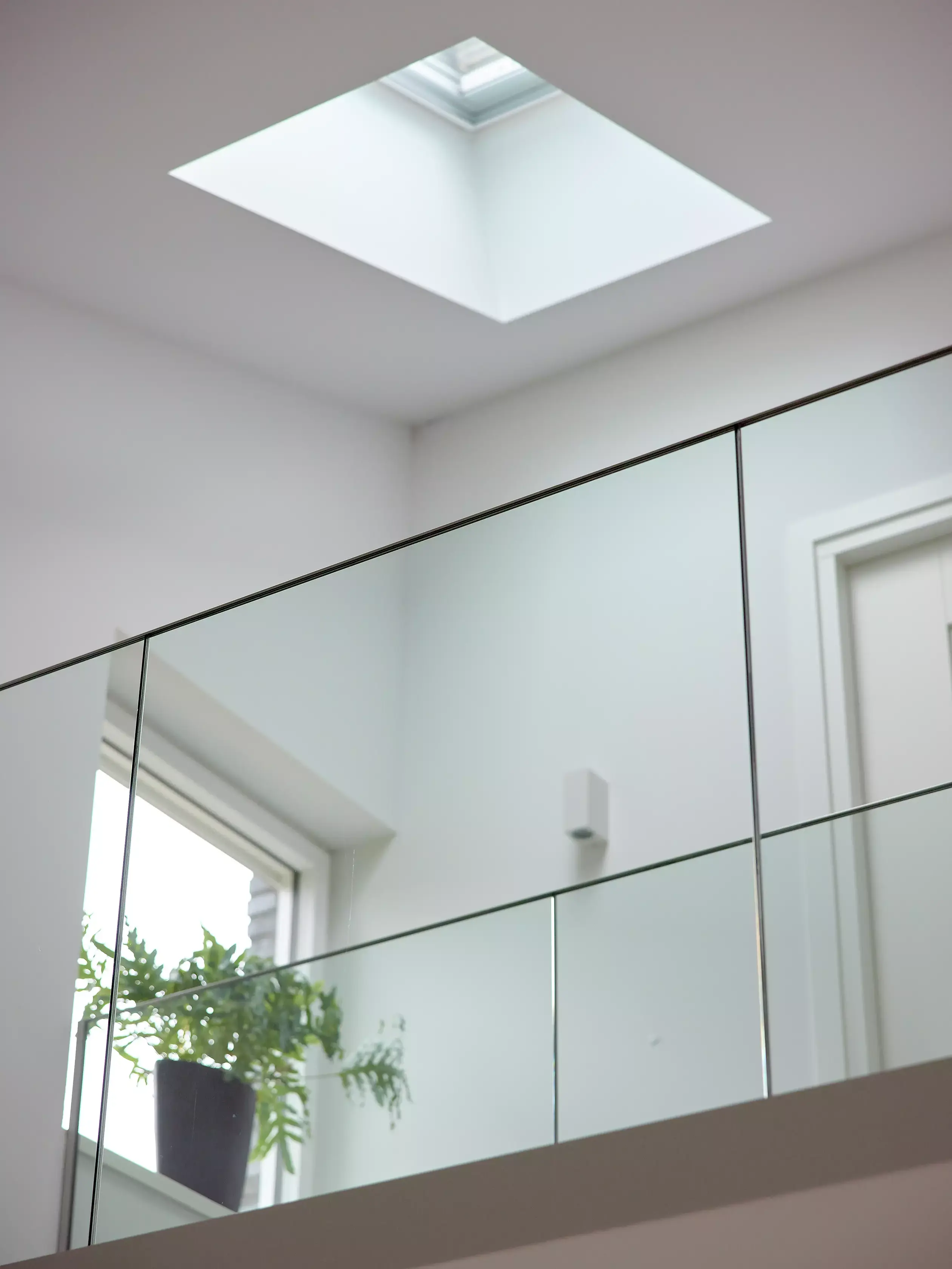 Intérieur minimaliste avec fenêtre de toit VELUX et balustrade en verre reflétant la lumière naturelle.