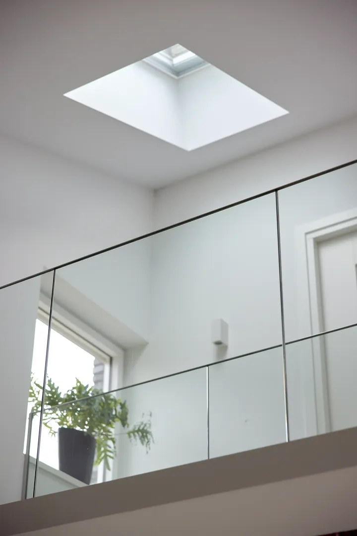 Svijetao, minimalistički interijer sa staklenom ogradom i velikim krovnim prozorom koji propušta prirodno svjetlo. Saksija s biljkom dodaje dašak zelenila modernom prostoru. | VELUX
