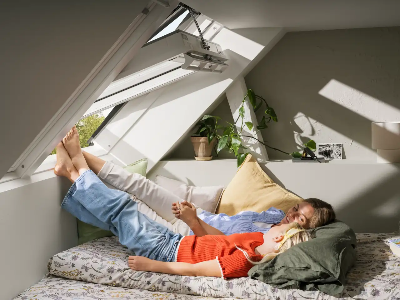 Une femme et une enfant allongées sur un lit, les pieds posés sur l’appui d’une fenêtre de toit VELUX ouverte 