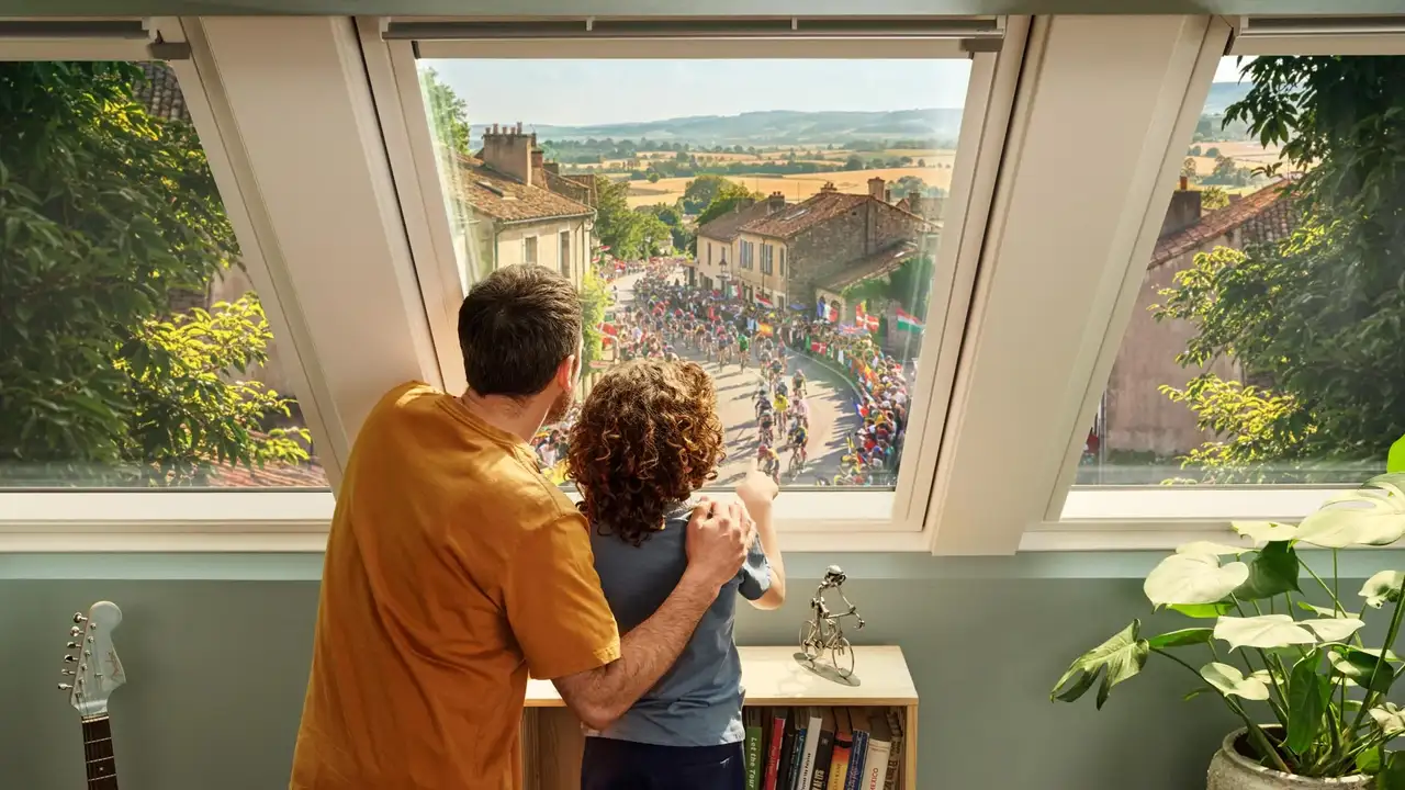 Oče in sin skozi strešno okno VELUX spremljata kolesarsko dirko.