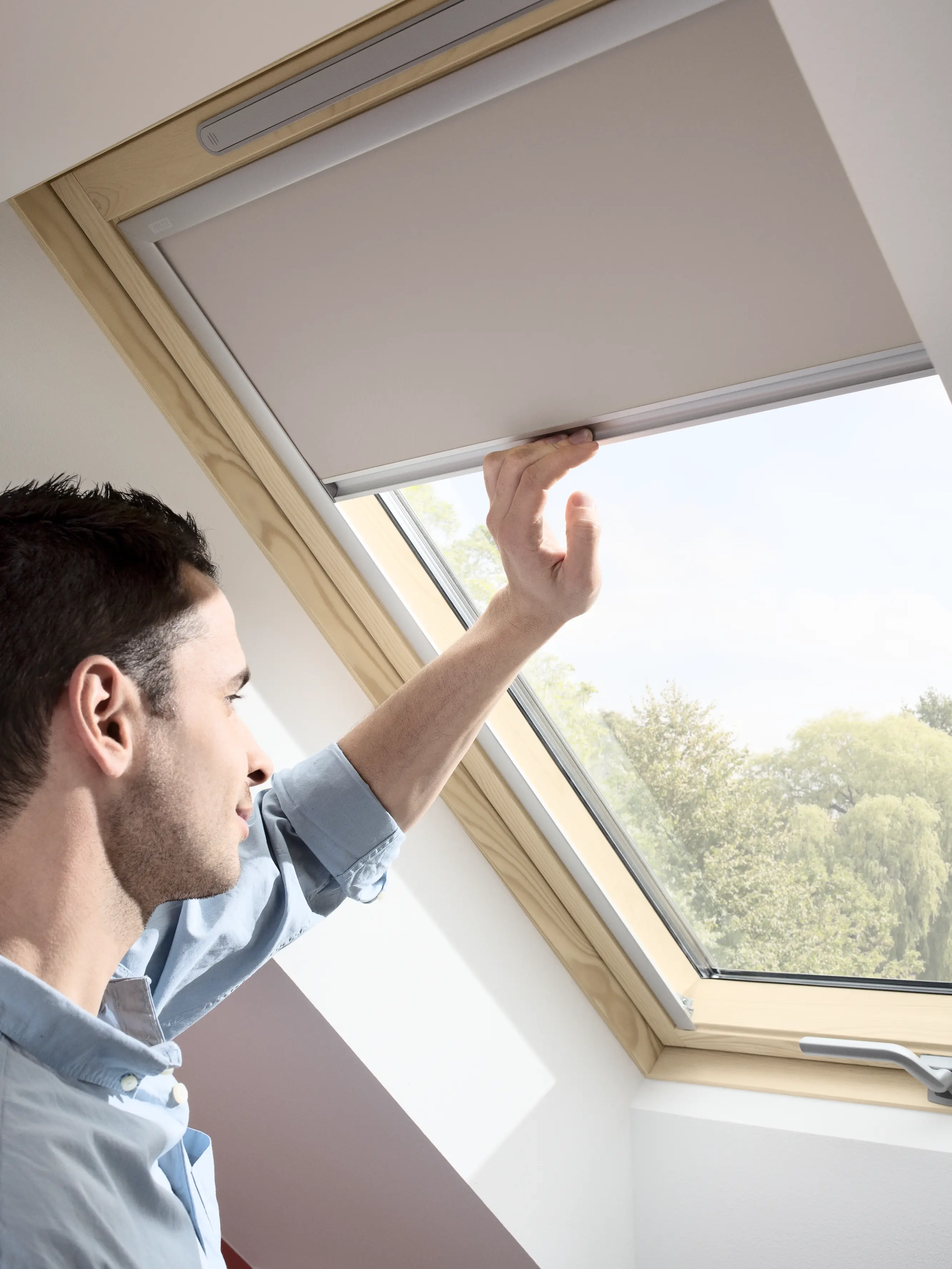 Person adjusting blind on VELUX roof window in attic room.