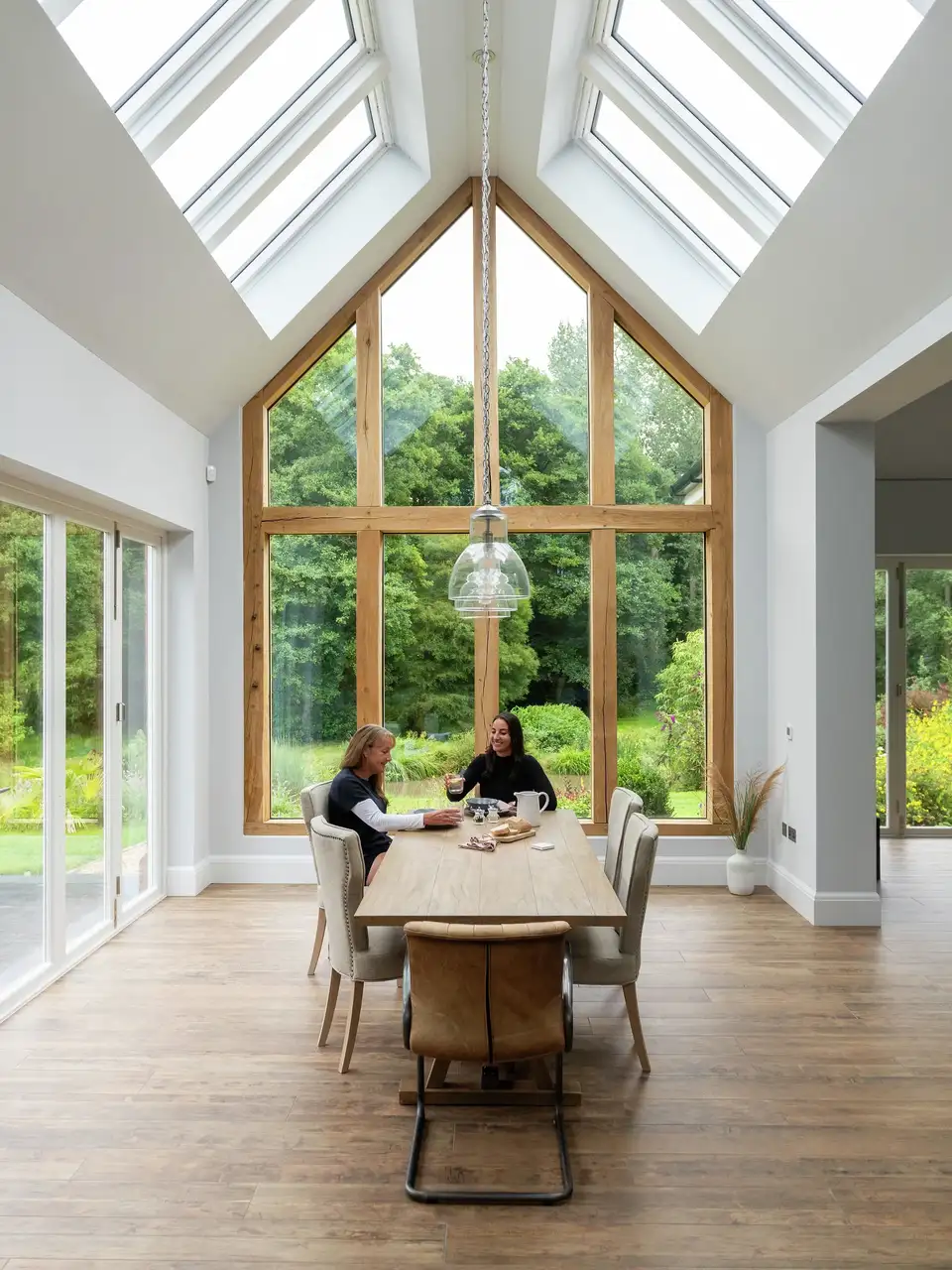 Sala da pranzo con grande tavolo, finestre da tetto VELUX e parete vetrata con vista sul giardino esterno. 