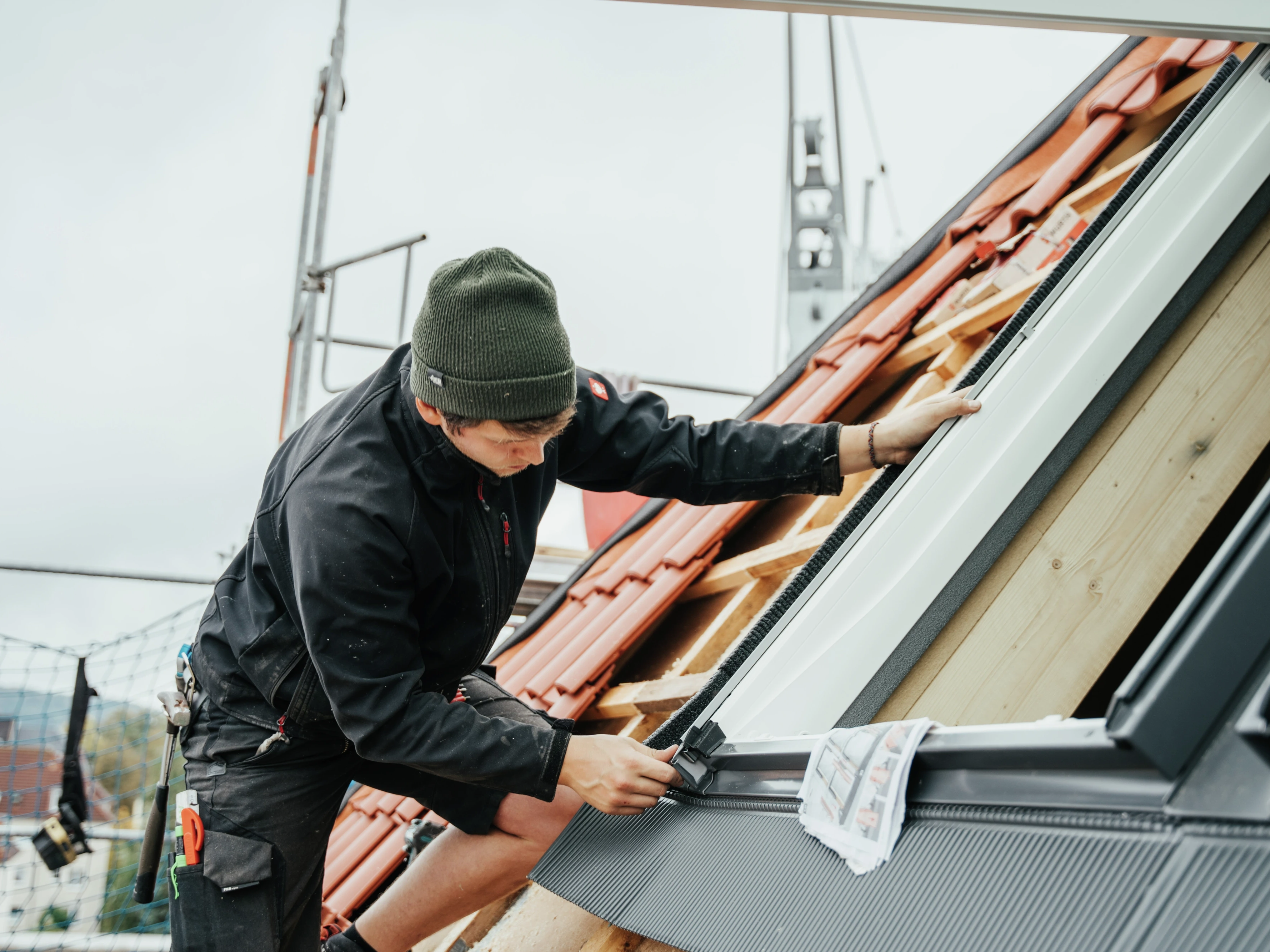 Работник монтира покривен прозорец VELUX на стръмен покрив с червени керемиди.