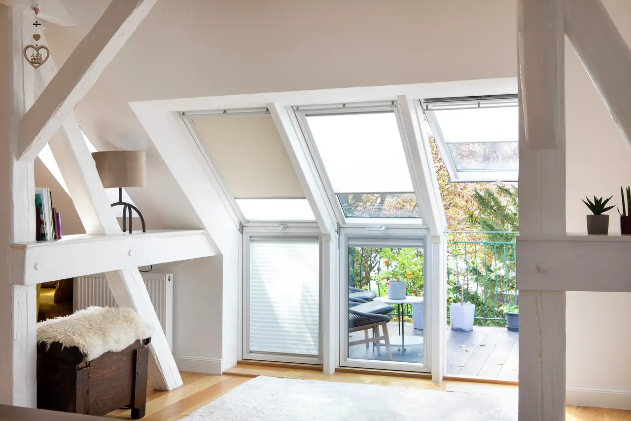 Cozy attic with roof windows, blinds, and a small balcony area with plants | VELUX