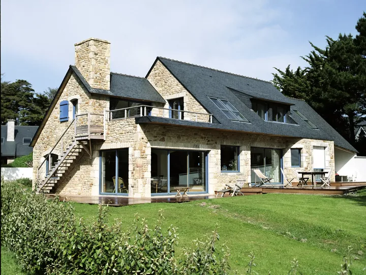 Steinhaus mit Schieferdach und VELUX Dachflächenfenstern, umgeben von Grünanlagen mit einer hölzernen Terrasse.