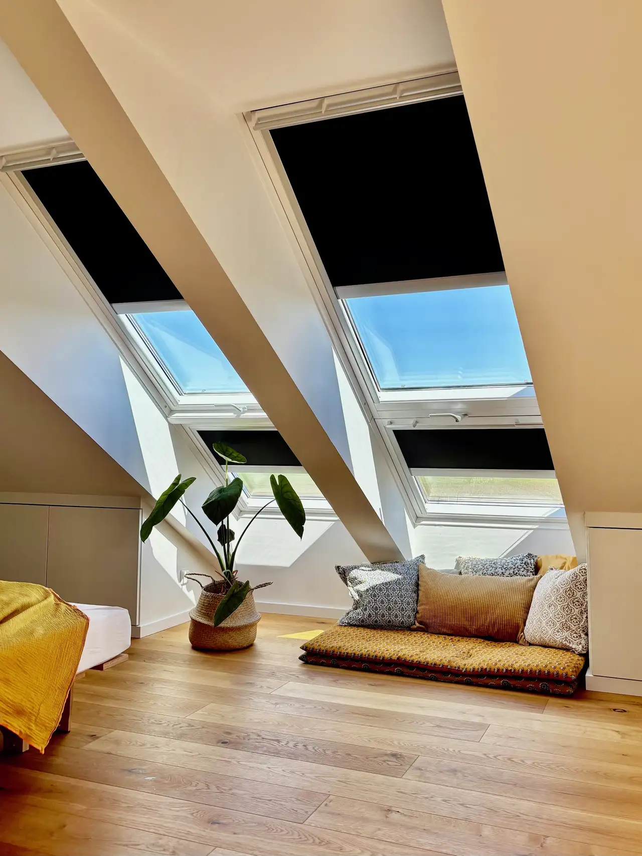Camera da letto in mansarda con zona relax disposta sotto grandi finestre per tetti schermate da tende colorate.
