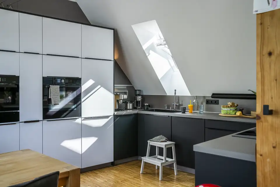 Cucina moderna in mansarda con piano di lavoro addossato a una parete perimetrale bassa e un mobile alto sulla parete alta.