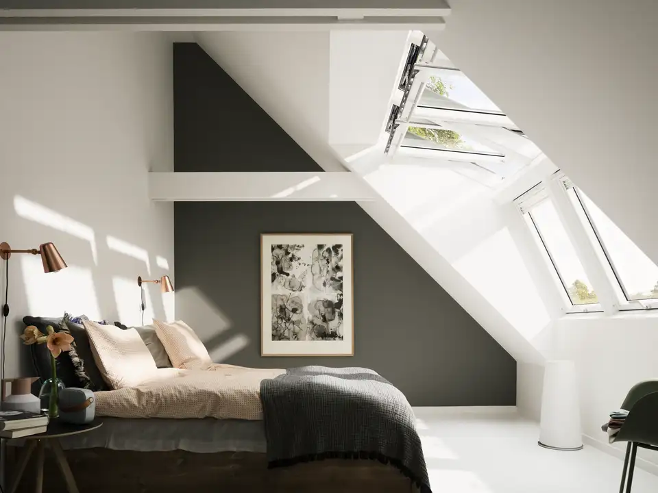 Attic bedroom with sloped ceiling and open VELUX roof windows, natural light entering. 