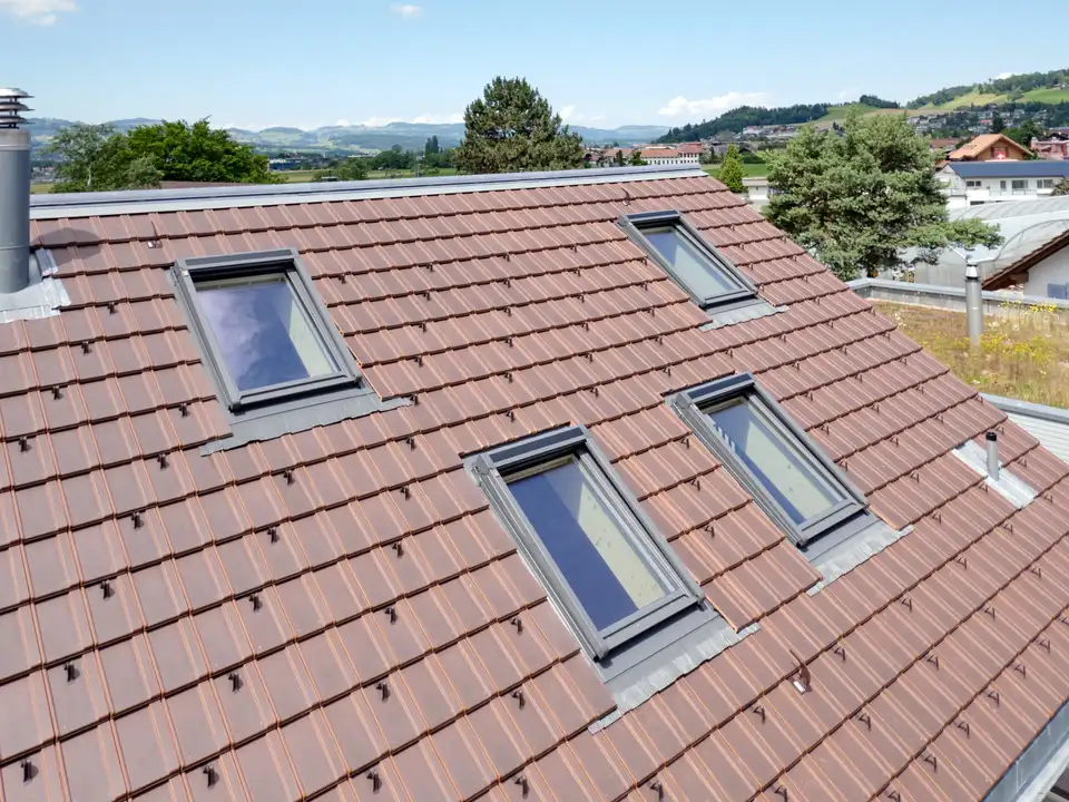 toit à deux pans avec tuiles rouges et quatre fenêtres de toit VELUX à hauteurs différentes 